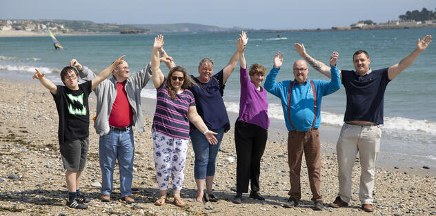 A group of people standing on a beach all happily raising their hands up in the air.